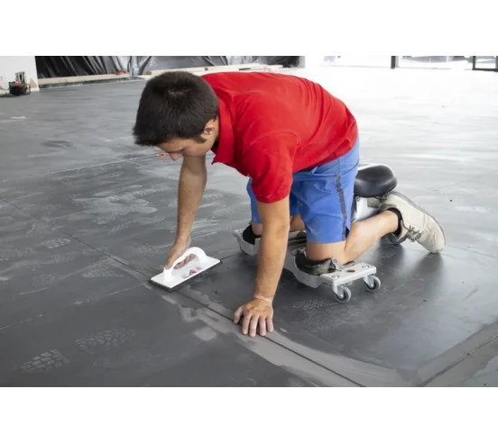 Carreleur utilisant le siège ergonomique SR-1 RUBI en situation, finition de joint au sol avec une taloche éponge.