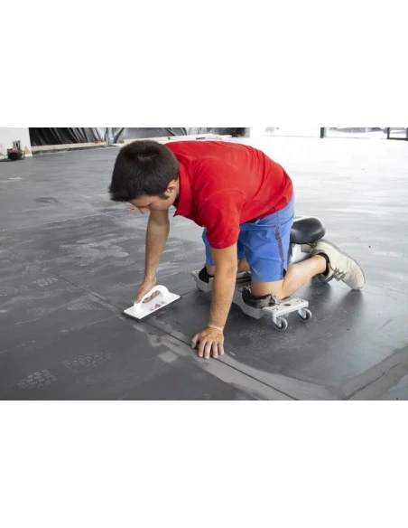 Carreleur utilisant le siège ergonomique SR-1 RUBI en situation, finition de joint au sol avec une taloche éponge.