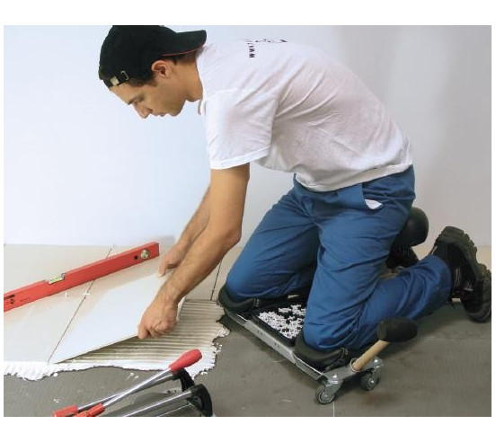 Carreleur en situation utilisant le Siège ergonomique SR-1 RUBI pour poser des carreaux au sol, vue latérale.